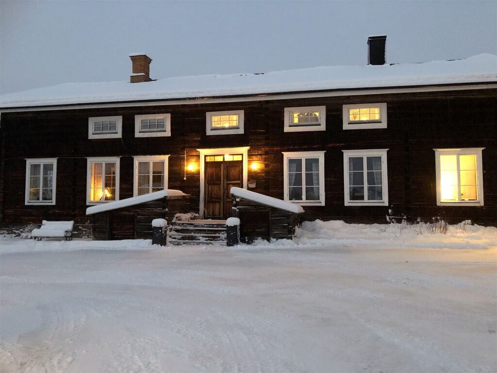 Det timrade huset från 1800-talet i snö, med ljus i fönstren